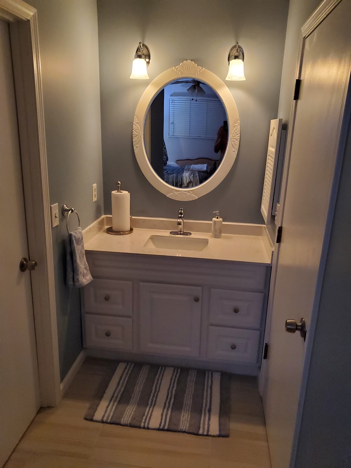 A finished bathroom with a blue vanity, oval mirror and tiled floor.