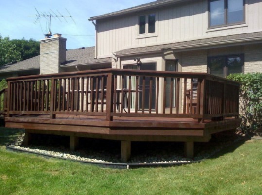 A cedar deck extends from a home beside a grassy yard.