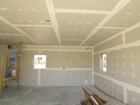 A wide unfinished room shows fresh drywall on the walls and ceiling.