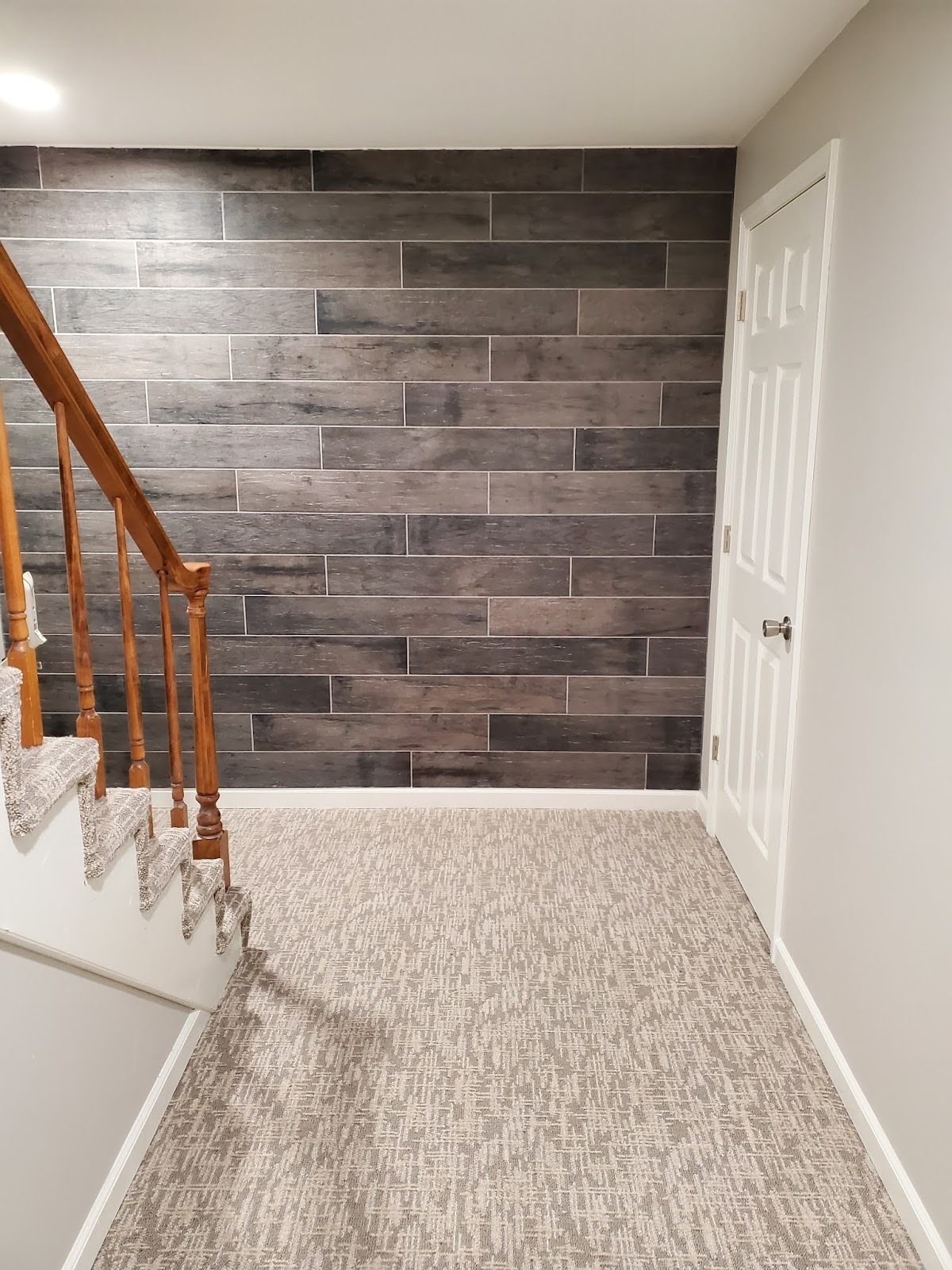 A finished basement stairway has carpeted steps and a gray tile accent wall.
